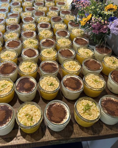 Viele Desserts im Glas in Reihen auf einem langen Holztisch, oben rechts ein Blumenstrauß